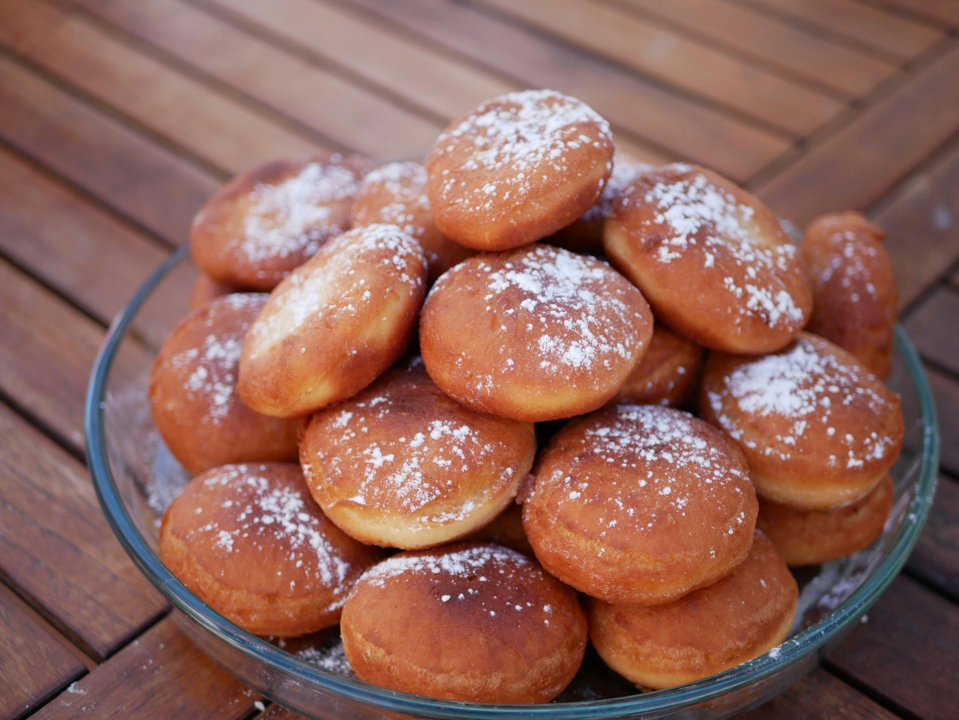 A plate of freshly baked homemade donuts sprinkled with powdered sugar on a wooden table.