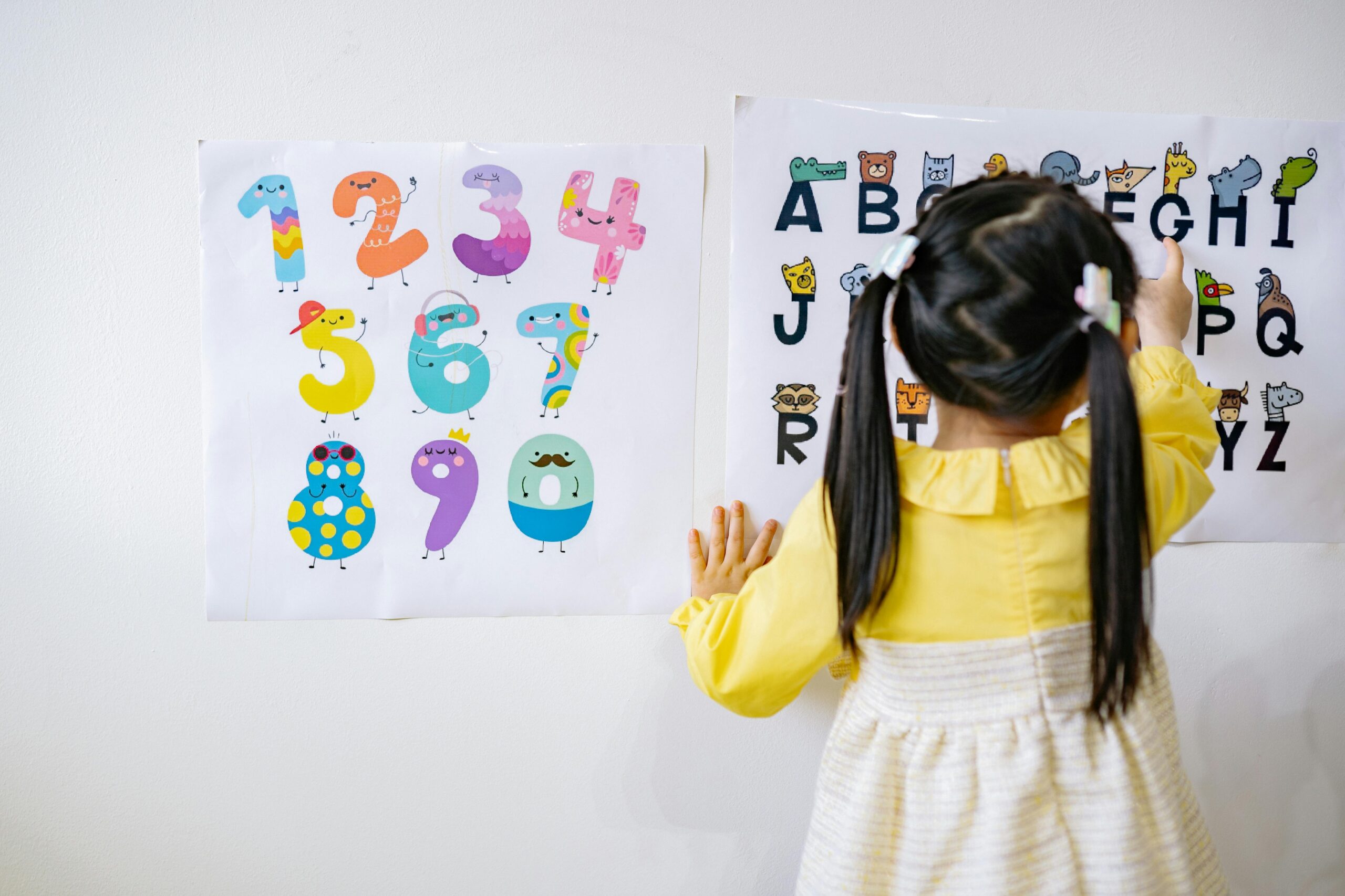 Young girl in kindergarten learning numbers and alphabets with colorful posters.