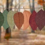 Fabric leaves hang on a rope, showcasing autumn colors in a forest backdrop.