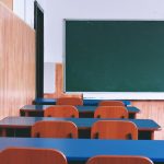 A serene view of an empty classroom with wooden desks, chairs, and a green chalkboard, capturing a quiet educational atmosphere.