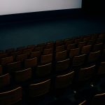 A dark and empty theater auditorium with rows of seats and a large screen.