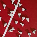A top-down view of shuttlecocks scattered on a red badminton court.